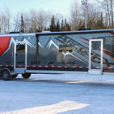 A snowmobile trailer with a custom vinyl wrap with red, black, and gray mountains and shapes.