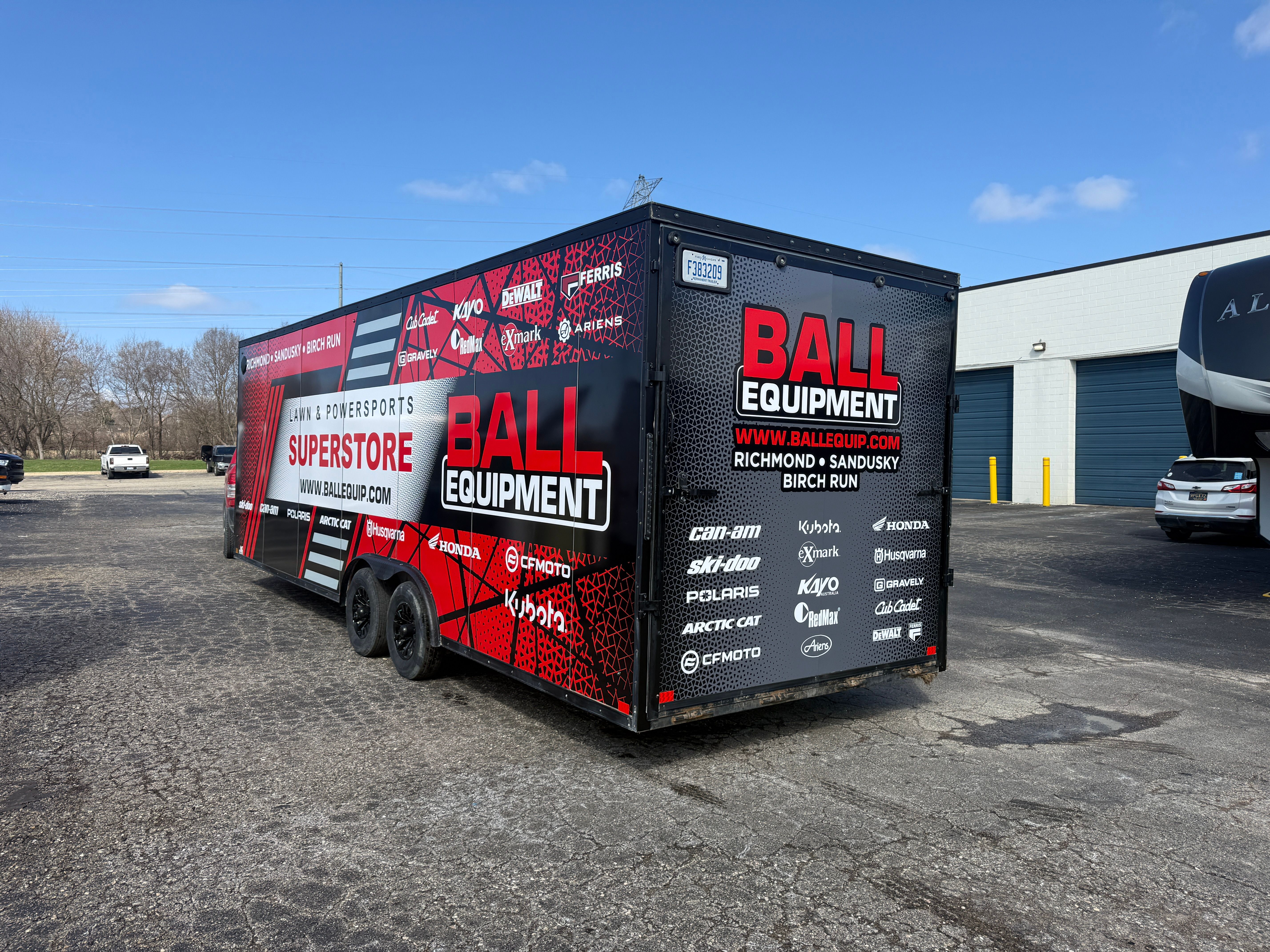 A commercial box trailer with a custom vinyl wrap with a red, black, and white logos and design