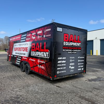 A commercial box trailer with a custom vinyl wrap with a red, black, and white logos and design
