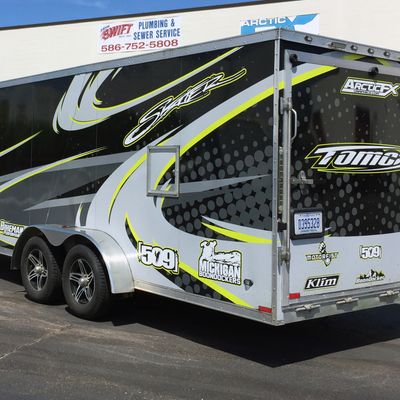 A snowmobile trailer with a custom decorative tribal vinyl wrap with lime, gray and black lines and swirls.