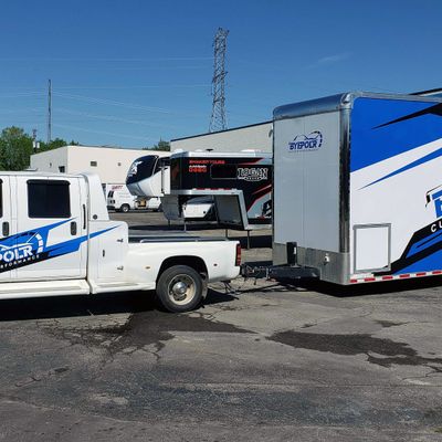 A commercial work truck and trailer with a custom vinyl wrap with white, black and blue shapes, logos, and stripes.