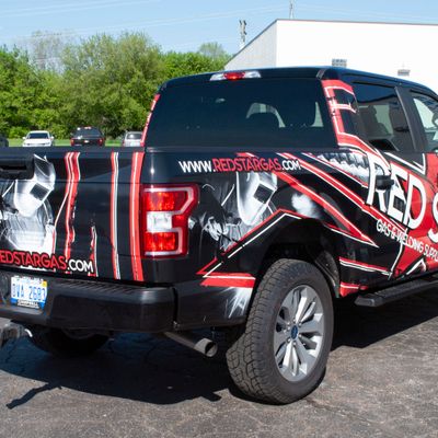 A commercial work truck with a custom vinyl wrap with red, white, and black logos and text with a grunge star design