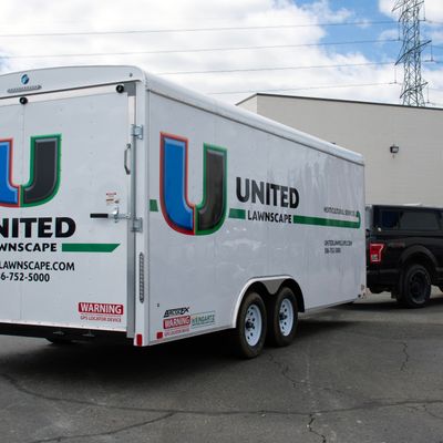 A commercial lawn service trailer with a custom vinyl wrap with white, green, and black logos and lines.