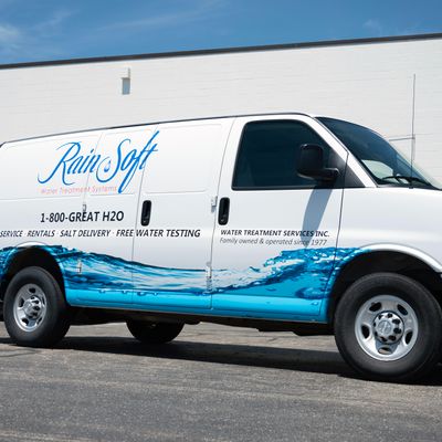 A commercial work van with a custom vinyl wrap with white, blue, and black text and logos with a water image