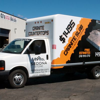 A commercial box truck with a custom vinyl wrap with orange, black, and white logos and simple grunge design