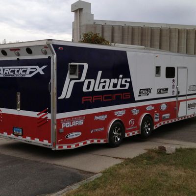 A snowmobile trailer with a custom vinyl wrap with white, blue, and red stripes and logos.