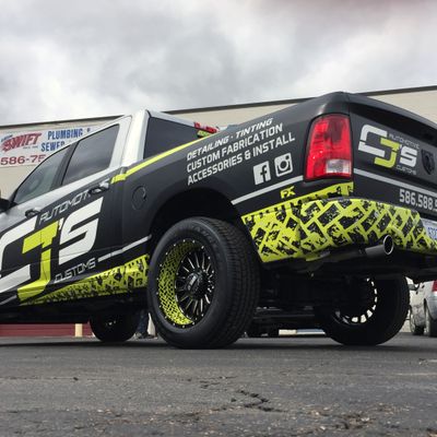 A commercial work truck with a custom vinyl wrap with lime green, white, and black logos and text with a grunge tire track design