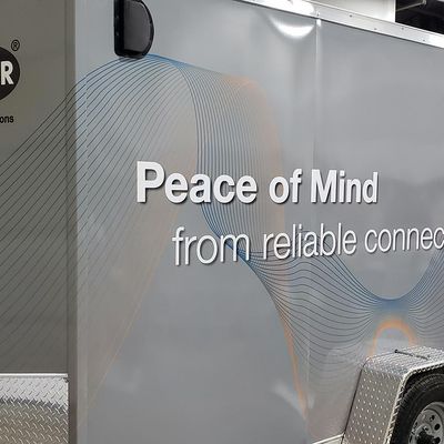 A commercial trailer with a custom vinyl wrap with gray, white, and black shapes and logos.