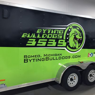 A commercial trailer with a custom vinyl wrap with lime green, black, and white logos and school design.