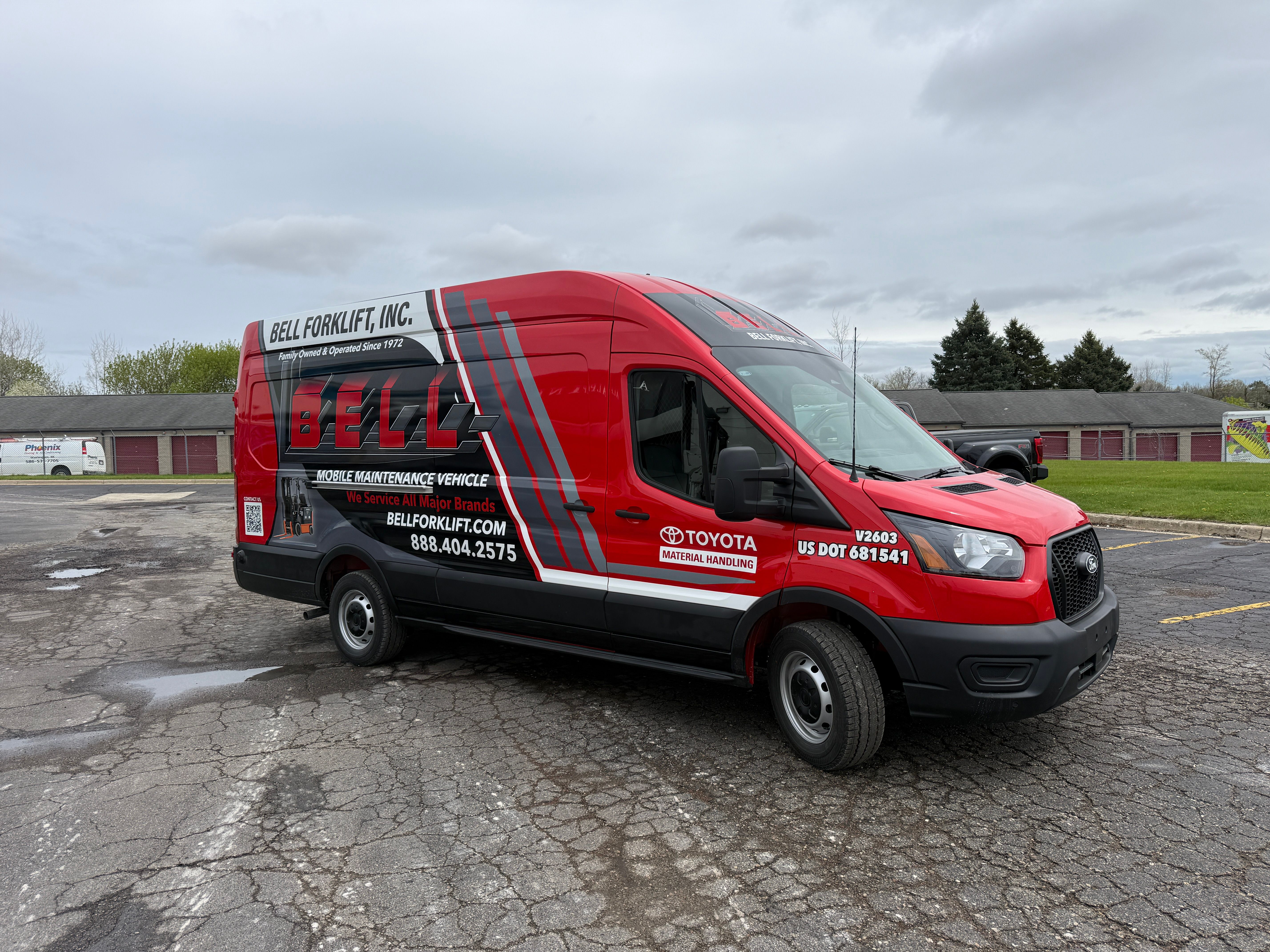 A commercial work van with a custom vinyl wrap with red, black, and grey logos and design