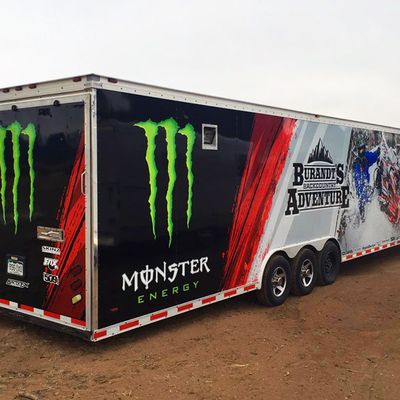 A snowmobile trailer with a custom vinyl wrap with red, white, and black shapes and logos.