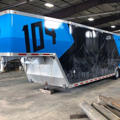 A snowmobile trailer with a custom vinyl wrap with blue, black, and gray sketch mountains and shapes.