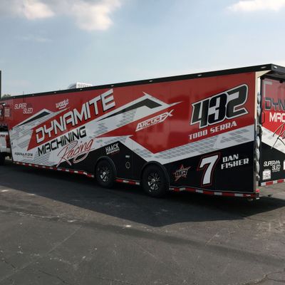 A snowmobile trailer with a custom vinyl wrap with black, red, and white shapes and patterns.