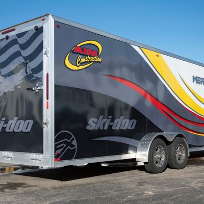 A snowmobile trailer with a custom vinyl wrap with yellow, white, gray and black tribal lines and swirls.