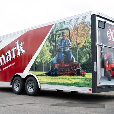 A commercial lawn service trailer with a custom vinyl wrap with red, white, and black logos and lines.