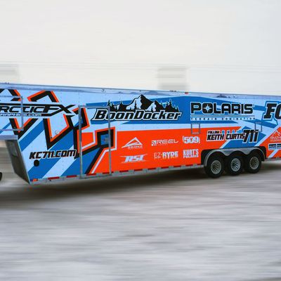 A snowmobile trailer with a custom vinyl wrap with bright orange, white and blue shapes and lines.