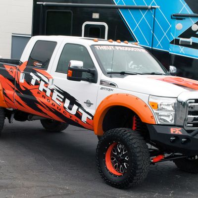 A commercial work truck with a custom vinyl wrap with orange, white, and black logos and text with a grunge design