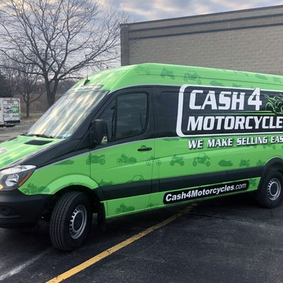 A commercial work van with a custom vinyl wrap with green, white, and black logos and text
