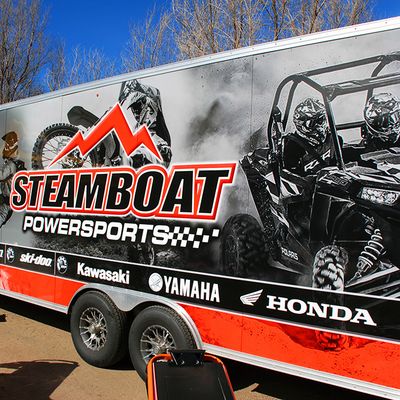 A snowmobile trailer with a custom vinyl wrap with red, white, and black lines and photographs.