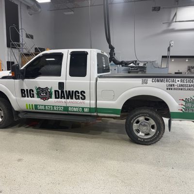 A commercial work truck with a custom vinyl wrap with black and green text and logo.