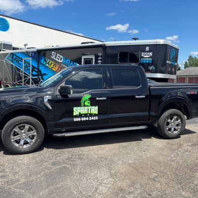 A commercial work truck with a custom vinyl wrap with green and white text and logo.