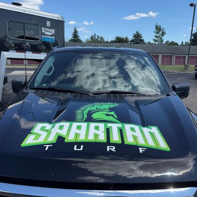 A commercial work truck with a custom vinyl wrap with green and white text and logo.
