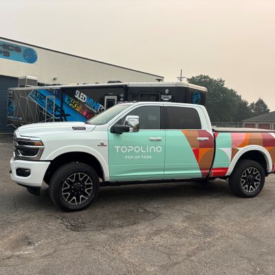 A commercial truck with a custom vinyl wrap with white text and geometric pattern.