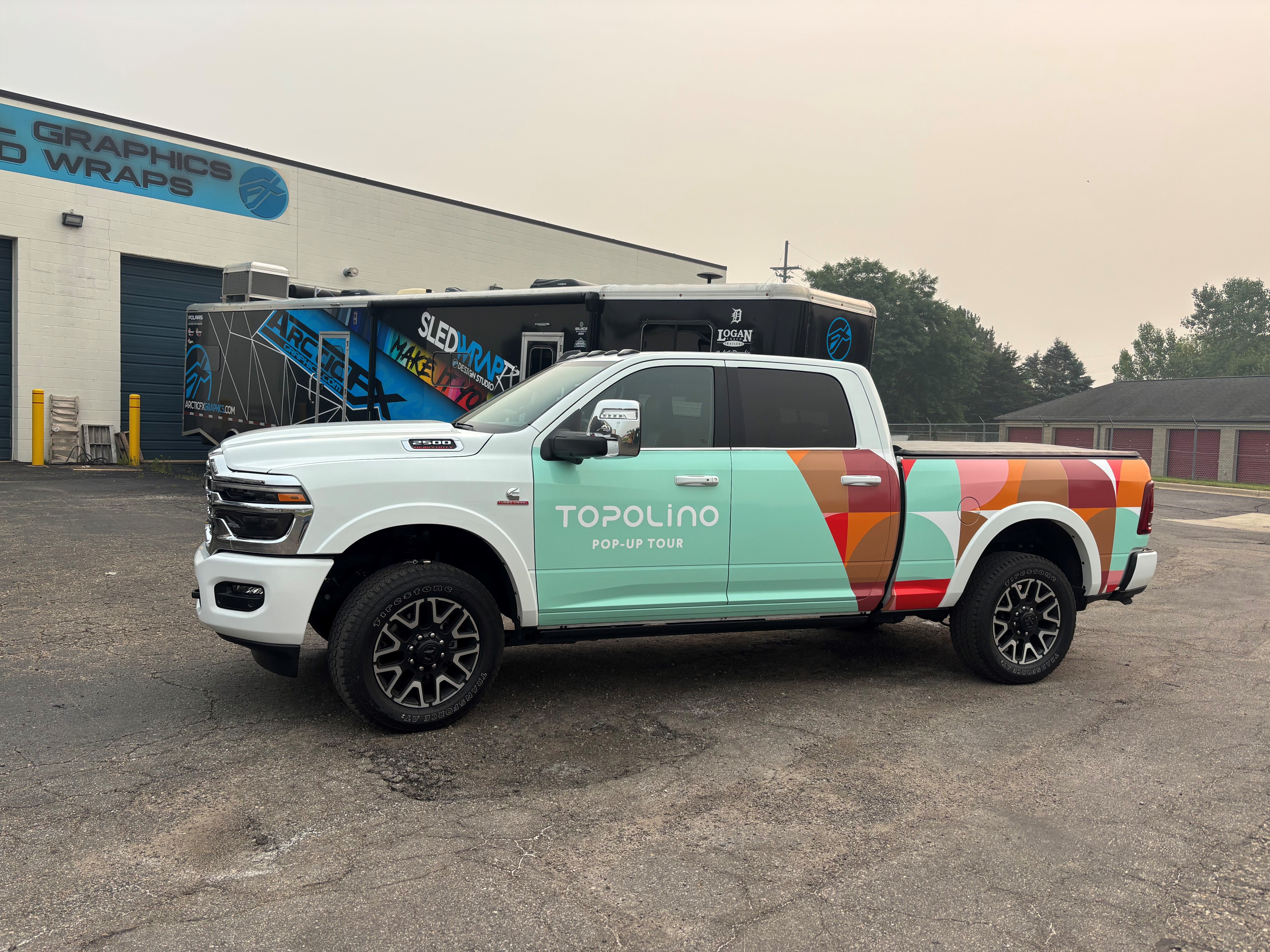 A commercial truck with a custom vinyl wrap with white text and geometric pattern.