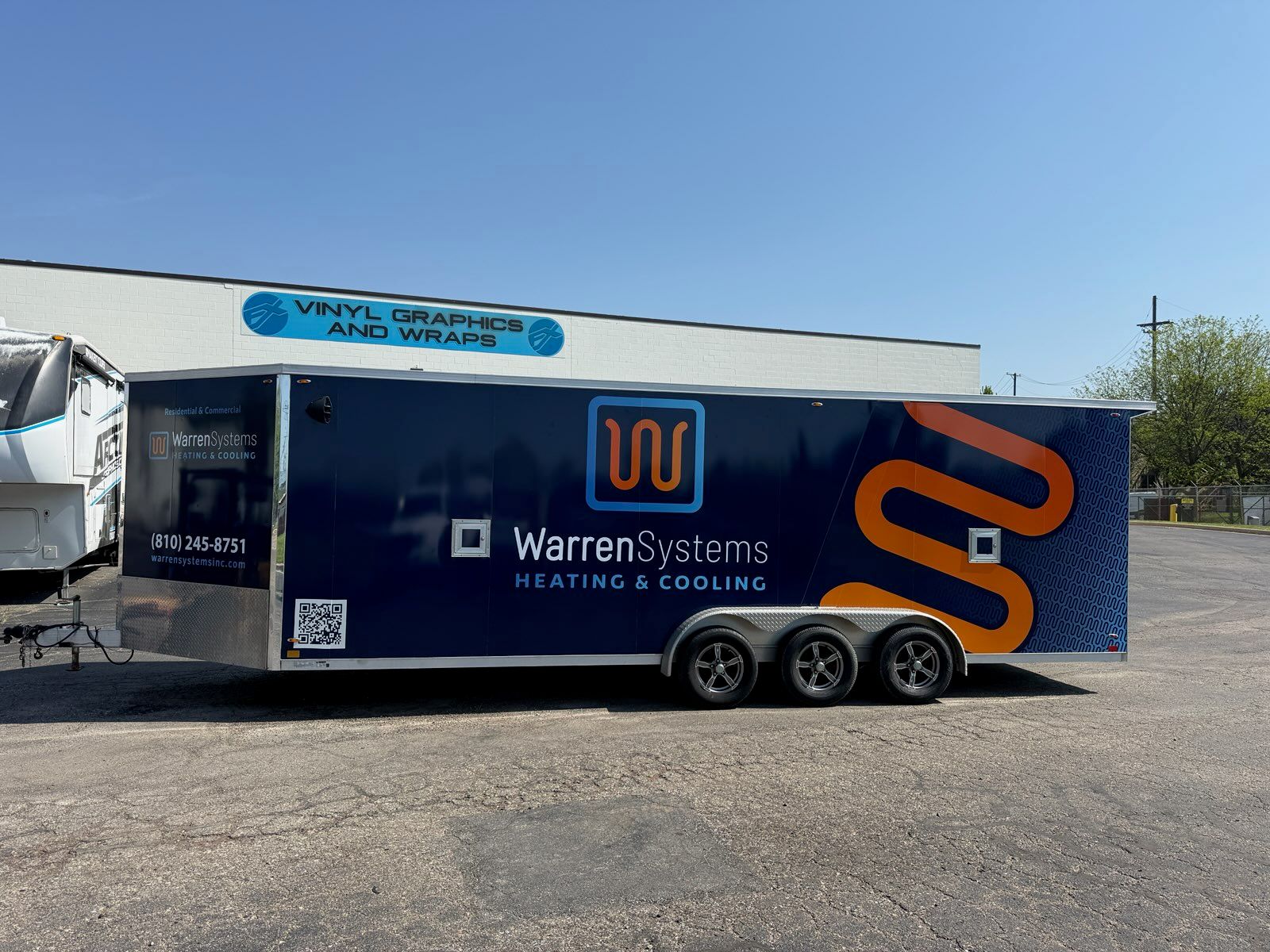 A commercial trailer with a custom vinyl wrap with blue, white, and orange logos.