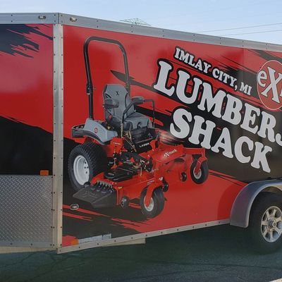 A commercial lawn service trailer with a custom vinyl wrap with red, black, and white logos and grunge shapes.