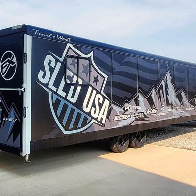 A snowmobile trailer with a custom vinyl wrap with black, gray, and white mountains and flags.