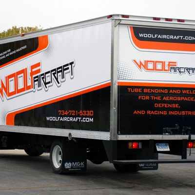A commercial box truck with a custom vinyl wrap with orange, black, and white logos and stripes