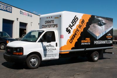 A commercial box truck with a custom vinyl wrap with orange, black, and white logos and simple grunge design