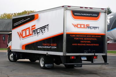 A commercial box truck with a custom vinyl wrap with orange, black, and white logos and stripes