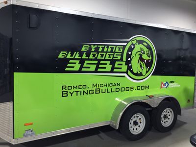 A commercial trailer with a custom vinyl wrap with lime green, black, and white logos and school design.