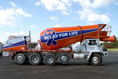 A commercial cement truck with a custom vinyl wrap of relay for life design colored purple and white ribbon and stripes on the barrel