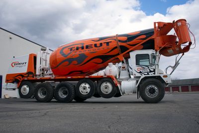 A commercial cement truck with a custom vinyl wrap of black and gray flames and logos on the barrel