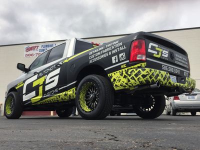 A commercial work truck with a custom vinyl wrap with lime green, white, and black logos and text with a grunge tire track design