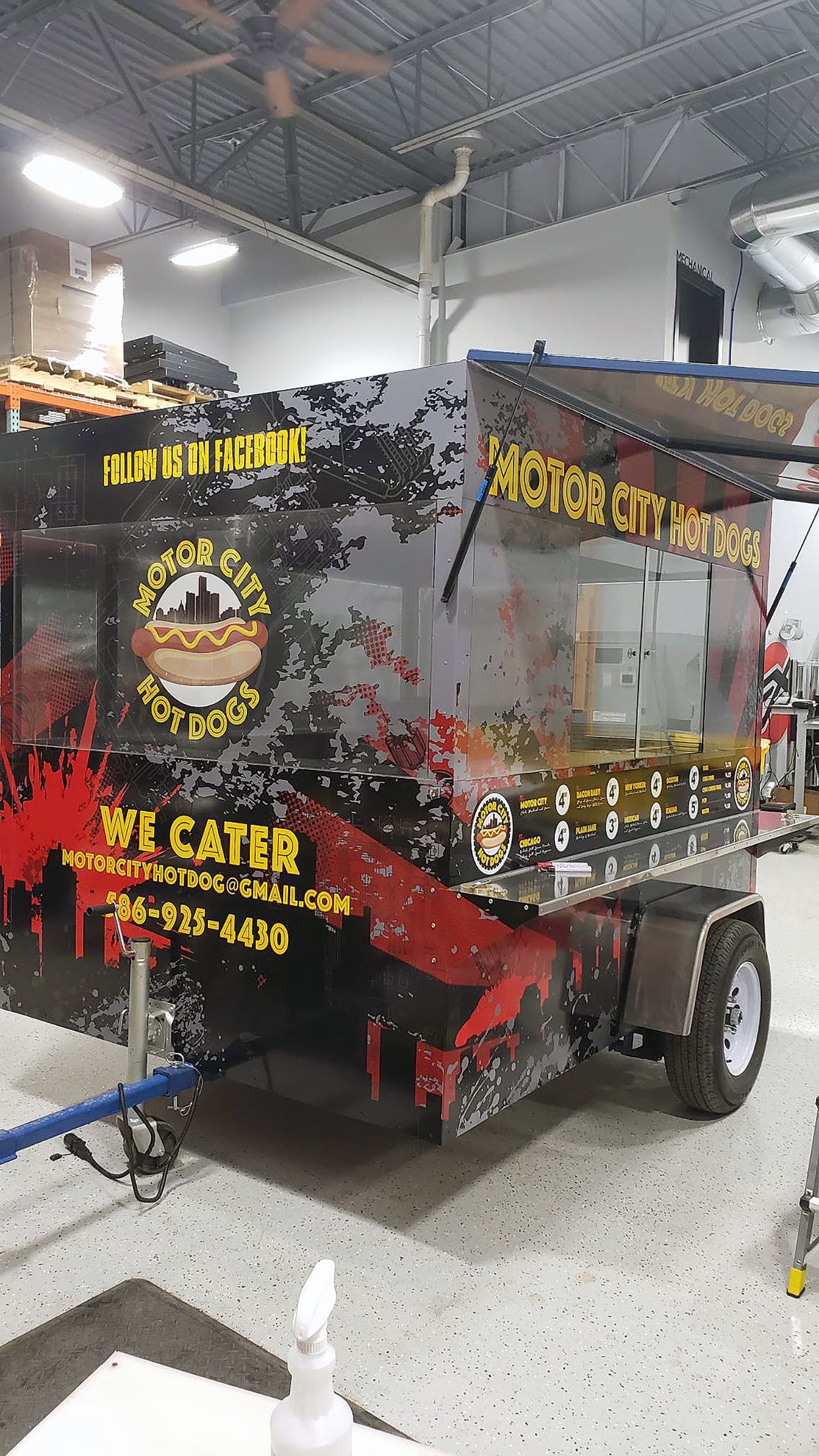 A commercial food hotdog truck with a custom vinyl wrap with yellow, red, and gray logos and text with a grunge city design.
