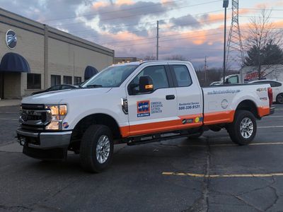 A commercial work truck with a custom vinyl wrap with orange, white, and blue logos and text