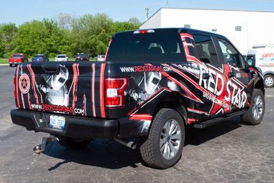 A commercial work truck with a custom vinyl wrap with red, white, and black logos and text with a grunge star design