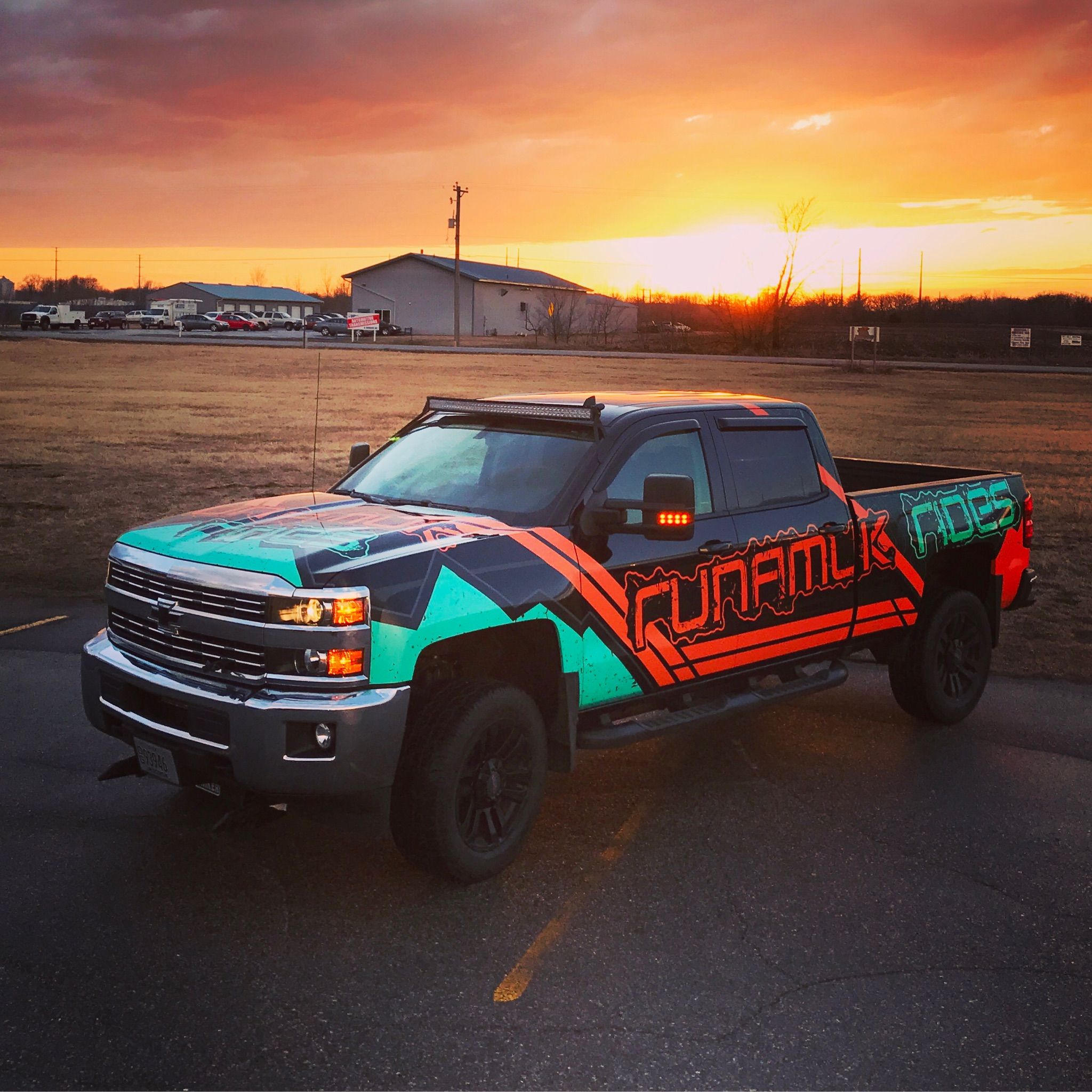 A commercial work truck with a custom vinyl wrap with orange, aqua, and black shapes and logos with stripes