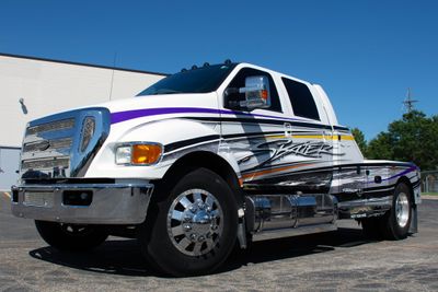 A commercial work truck with a custom vinyl wrap with purple, white, and black logos and text with a stripe design