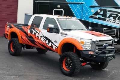 A commercial work truck with a custom vinyl wrap with orange, white, and black logos and text with a grunge design