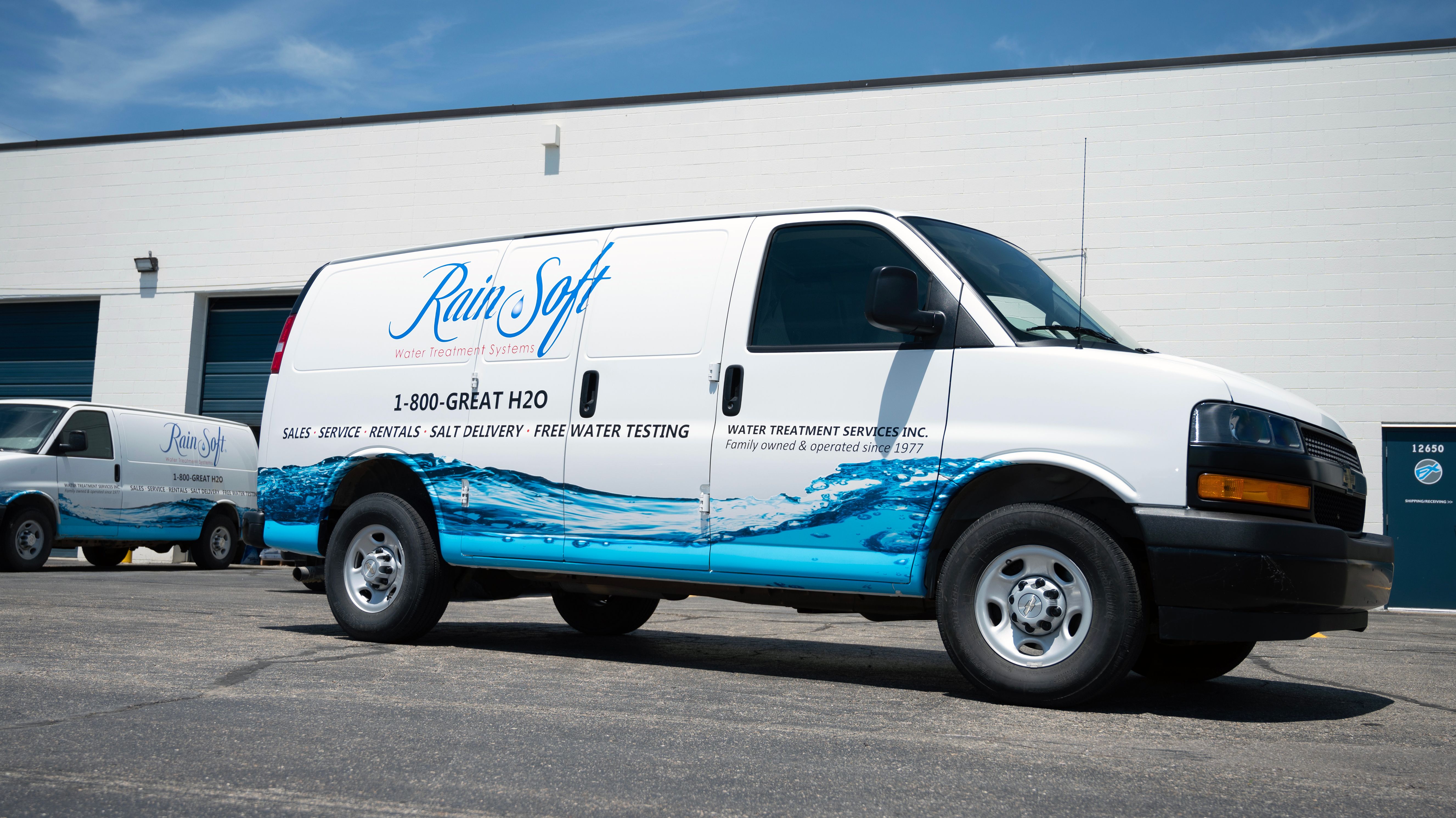 A commercial work van with a custom vinyl wrap with white, blue, and black text and logos with a water image