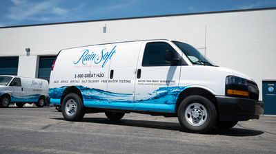 A commercial work van with a custom vinyl wrap with white, blue, and black text and logos with a water image