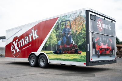 A commercial lawn service trailer with a custom vinyl wrap with red, white, and black logos and lines.