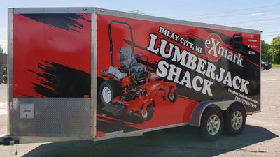 A commercial lawn service trailer with a custom vinyl wrap with red, black, and white logos and grunge shapes.