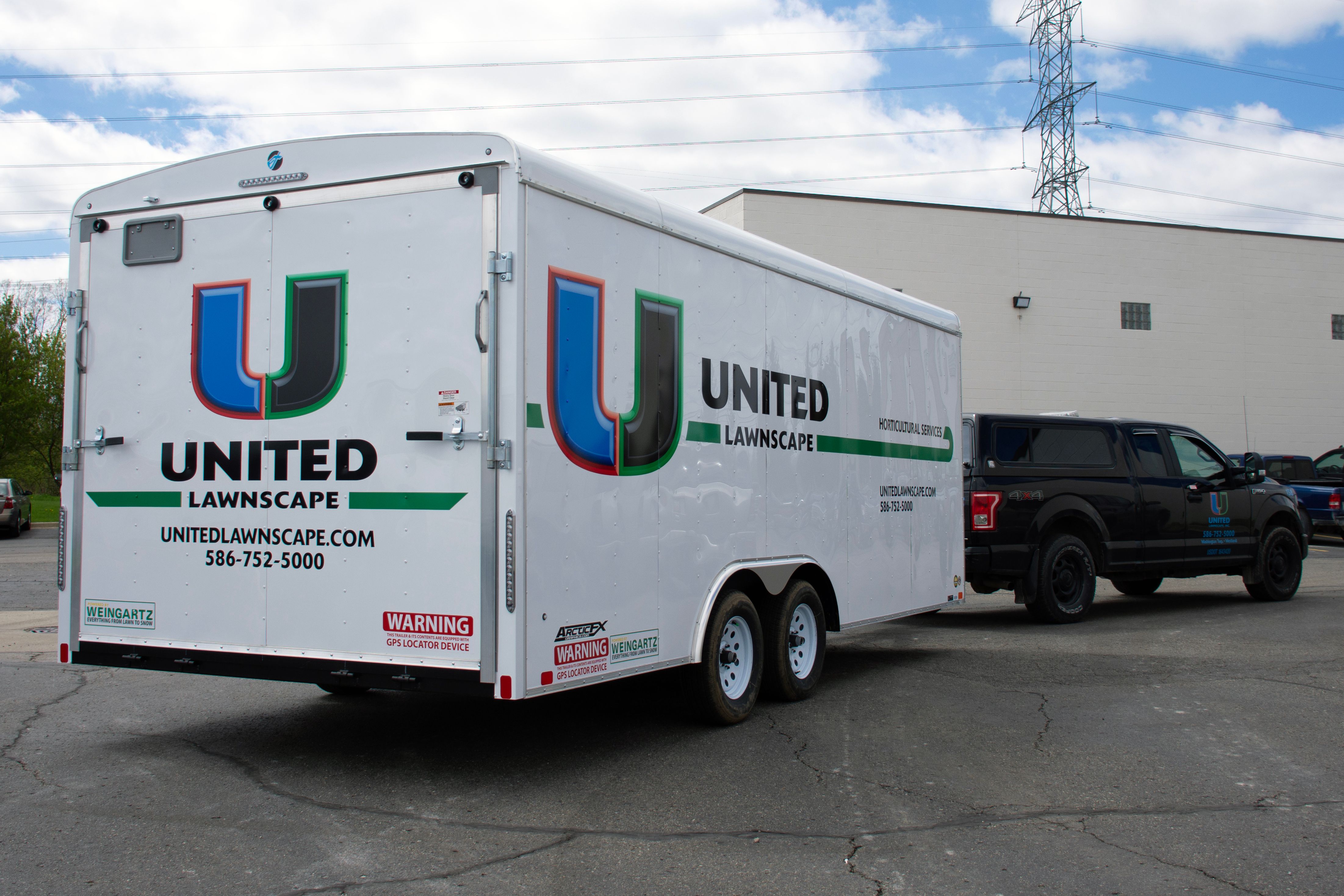 A commercial lawn service trailer with a custom vinyl wrap with white, green, and black logos and lines.