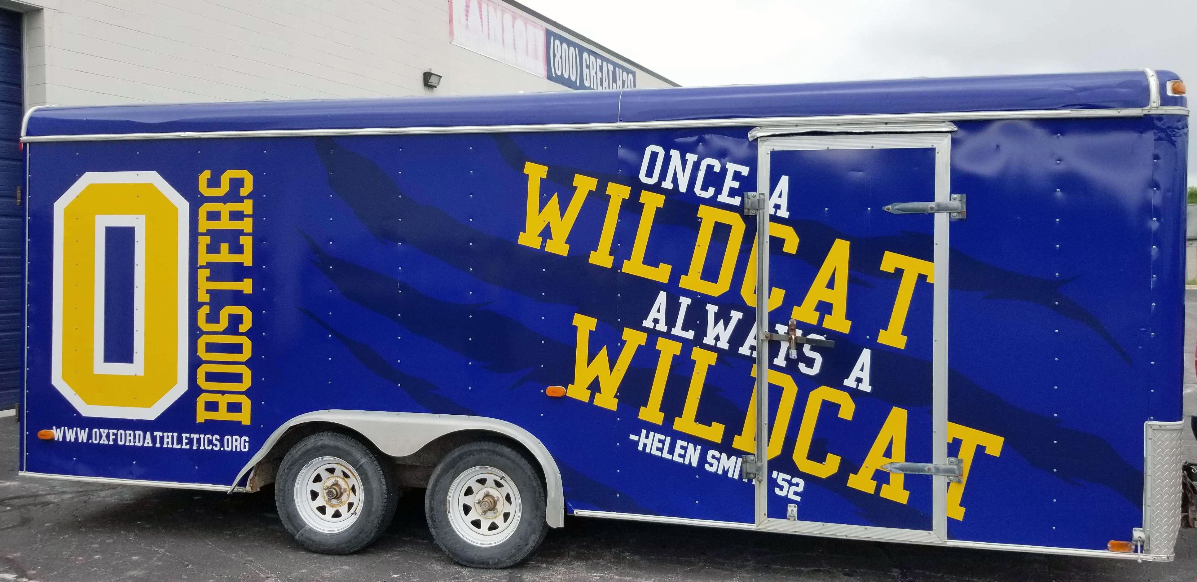 A commercial trailer with a custom vinyl wrap with yellow, blue, and white logos and school design.